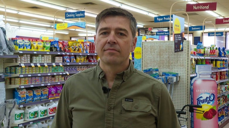 A man in his 40s wearing a green dress shirt stands in front of the drug history shelves.