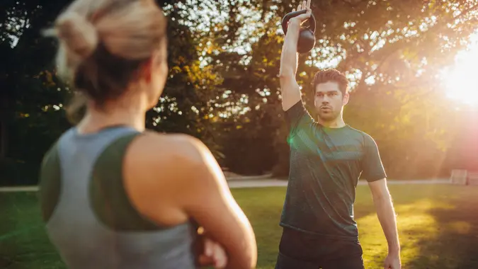 Young healthy boy with female trainer exercising with kettlebell in park.